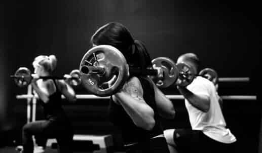 A group of people perform exercises with barbells across their shoulders